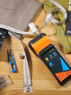 A collection of sewing tools and fabrics with a payment terminal on a wooden desk.
