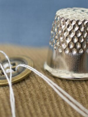 Photo by Marek Ruczaj A detailed macro shot of a sewing button and thimble on fabric, illustrating tailoring tools.