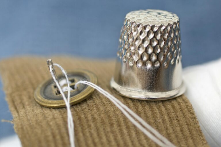 A detailed macro shot of a sewing button and thimble on fabric, illustrating tailoring tools.