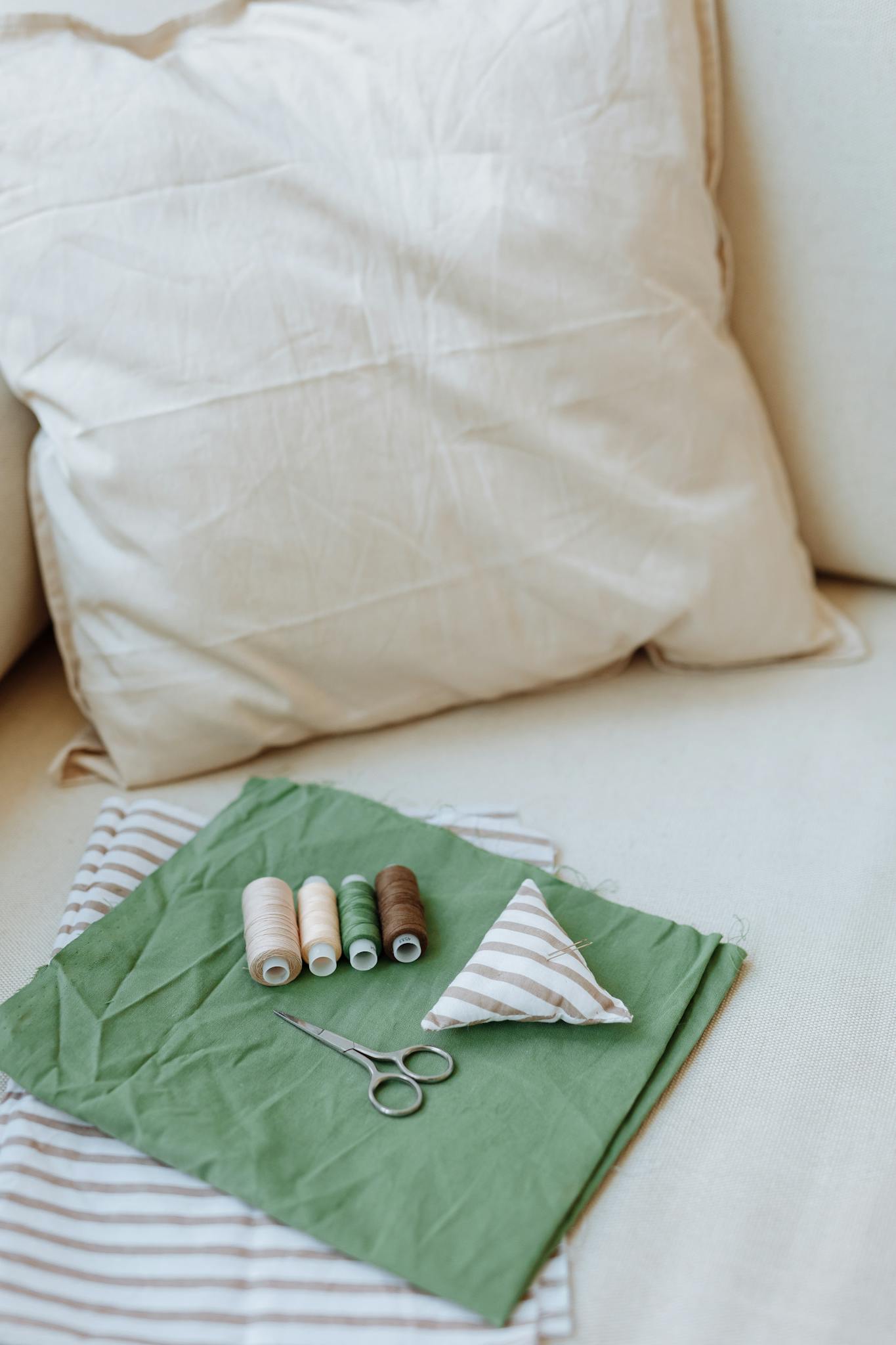 A detailed view of sewing supplies including fabric, threads, and scissors on a cushion.