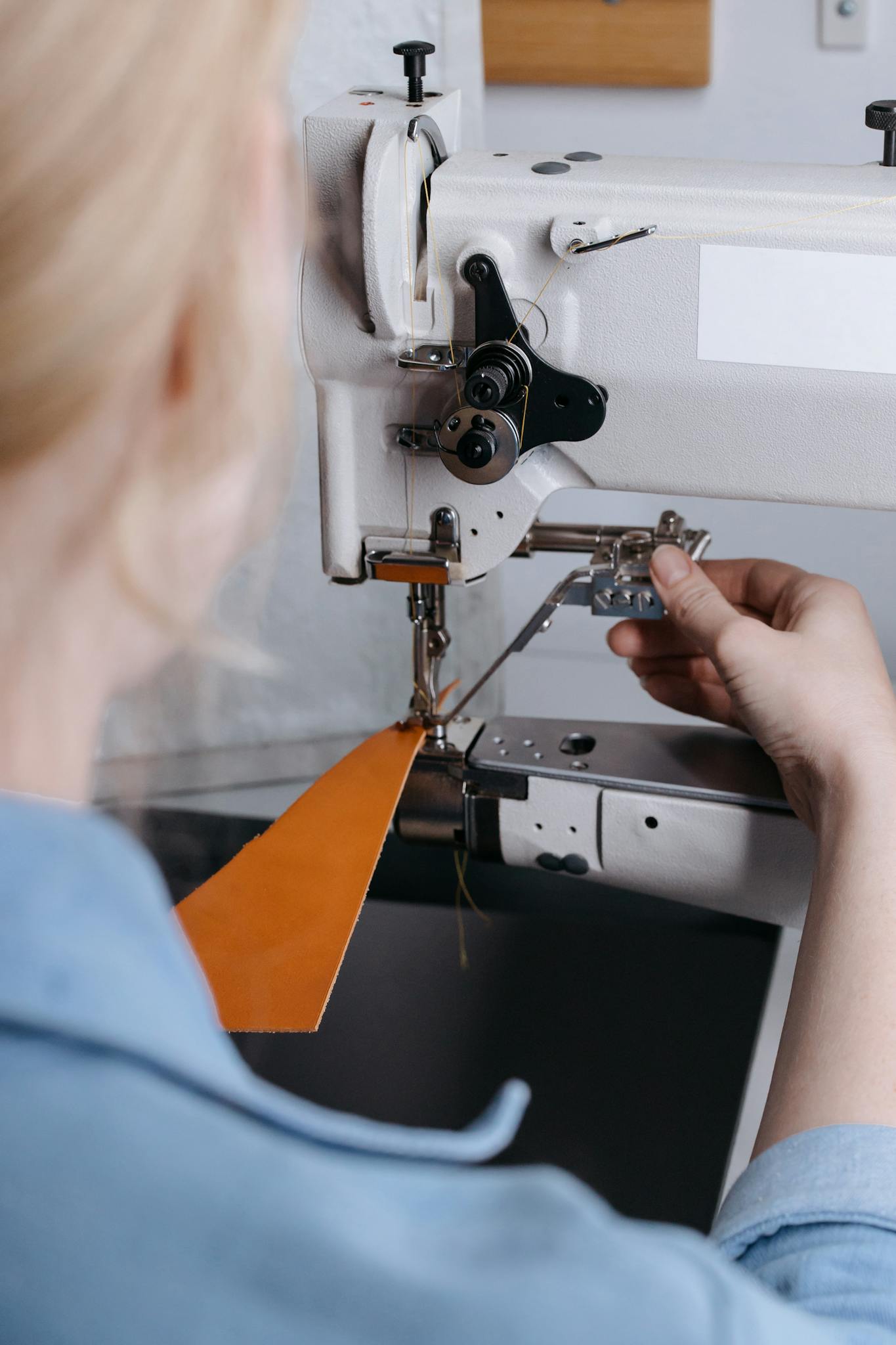 A person sewing leather with a machine in a workshop, focusing on the stitching process.