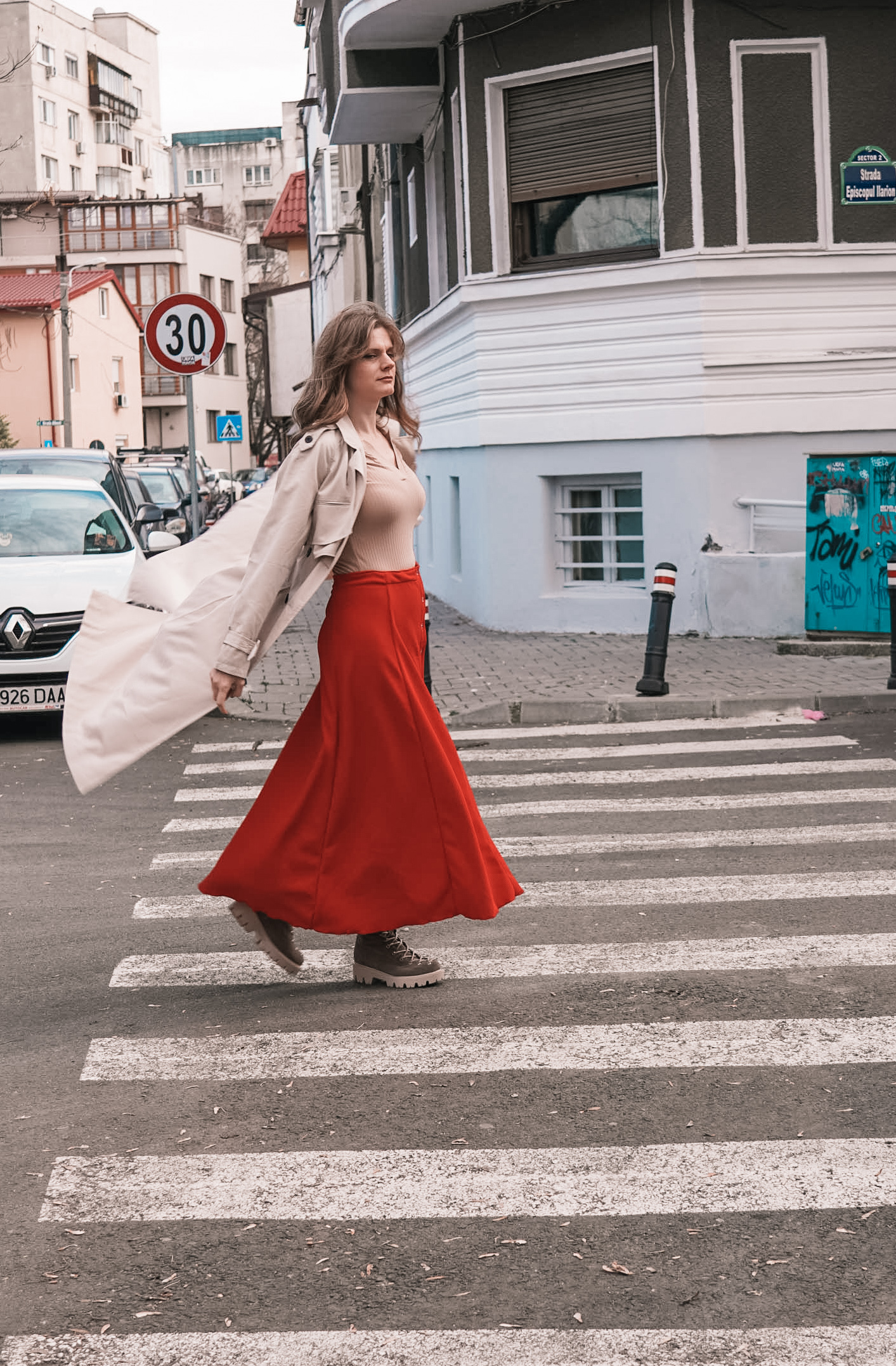90s A-Line Skirt in red ribbed knit walking across a city street, coat flying open