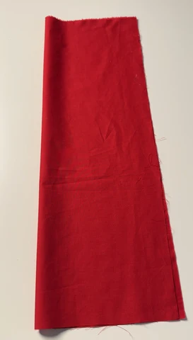 Red fabric rectangle cut for the bow loops, laid flat on a white surface