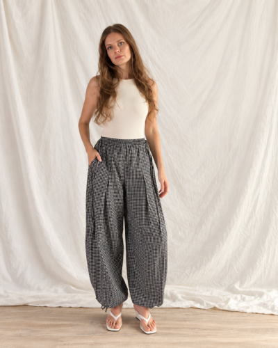 Jasmine balloon pants sewn in a black and white gingham check, worn with a white tank top, hands in the pockets