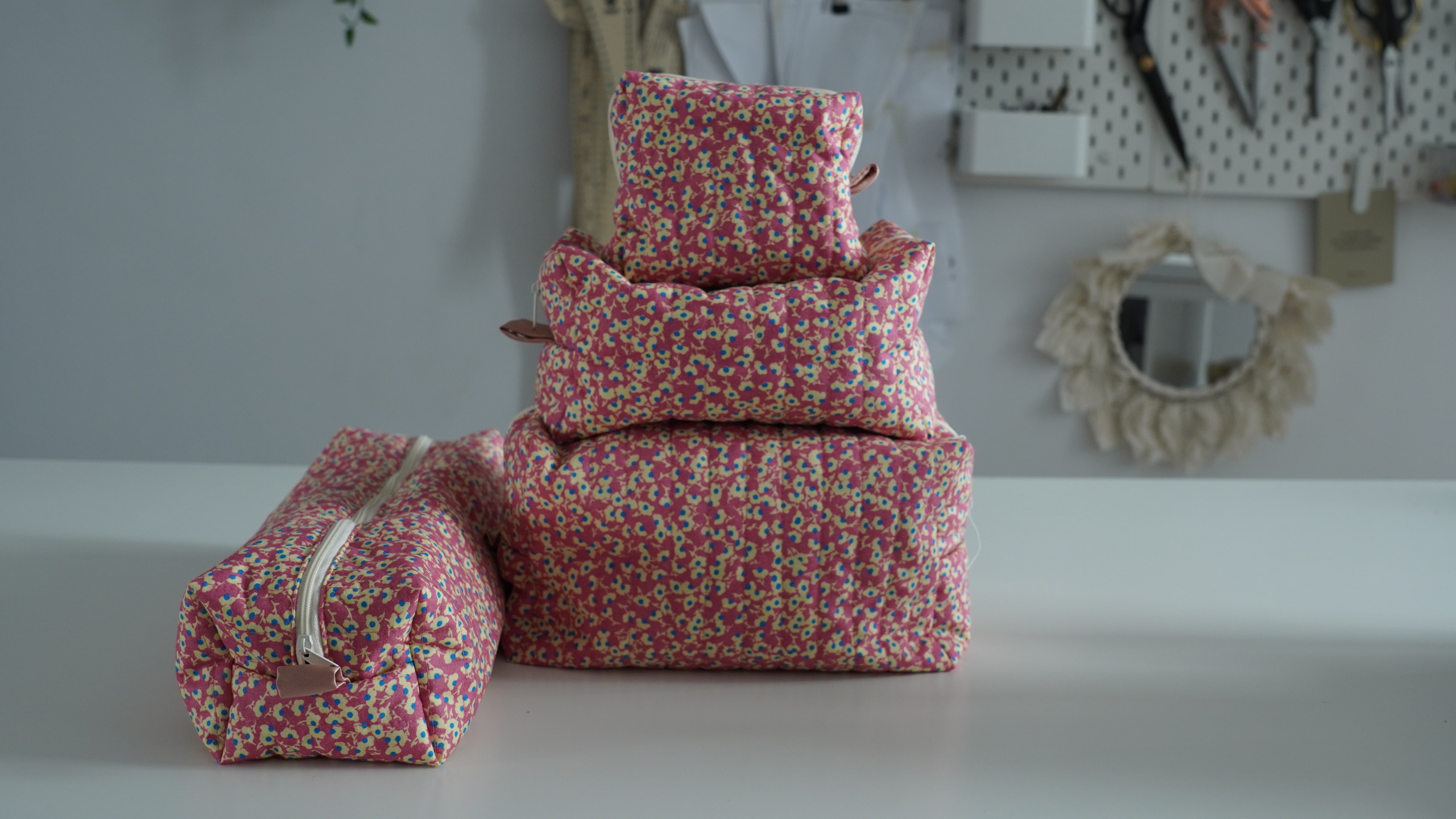 Quilted makeup bags in pink floral print stacked to show the size difference