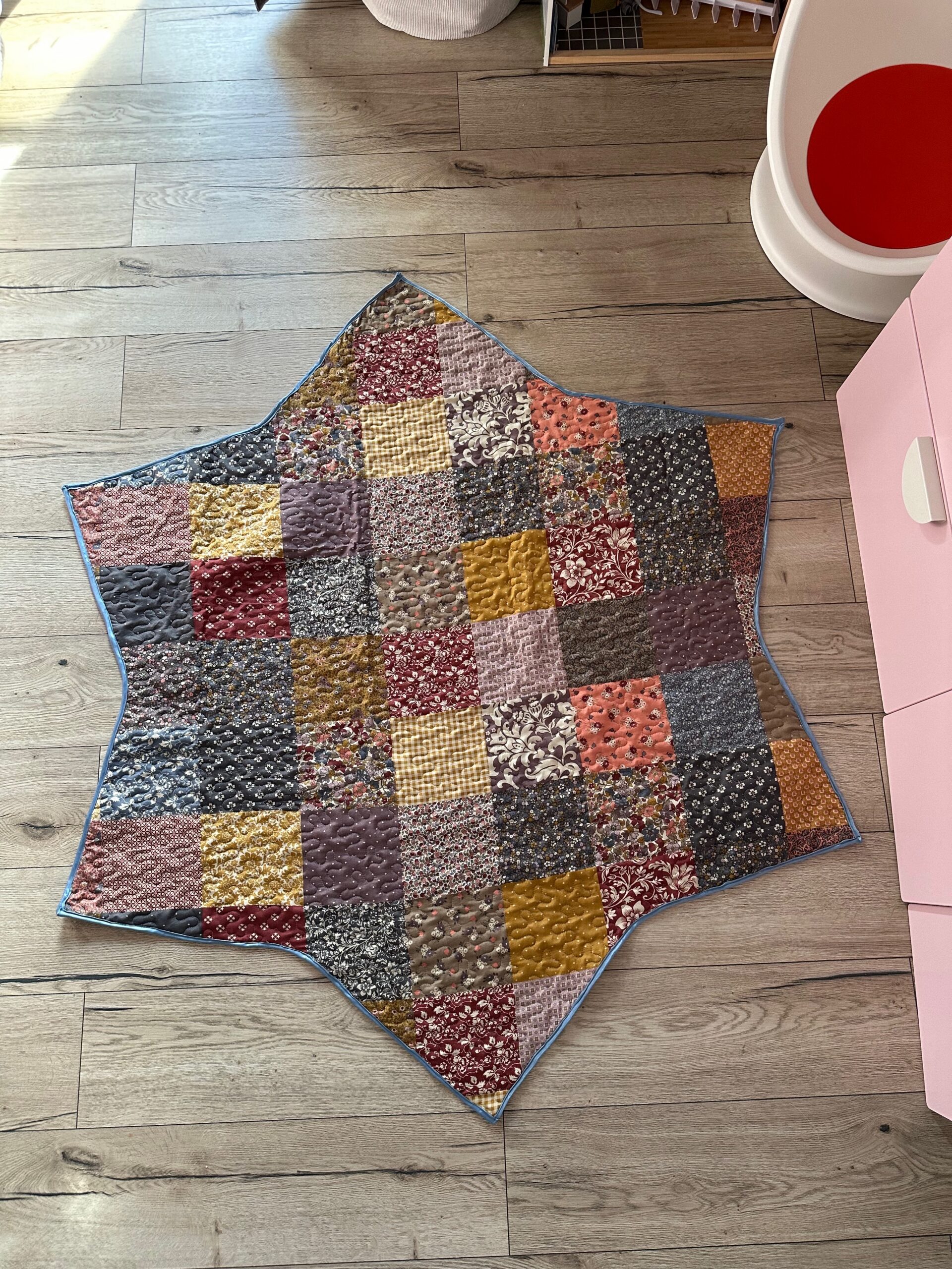 Patchwork version of the quilted tree skirt in mixed prints, laid out on a wooden floor