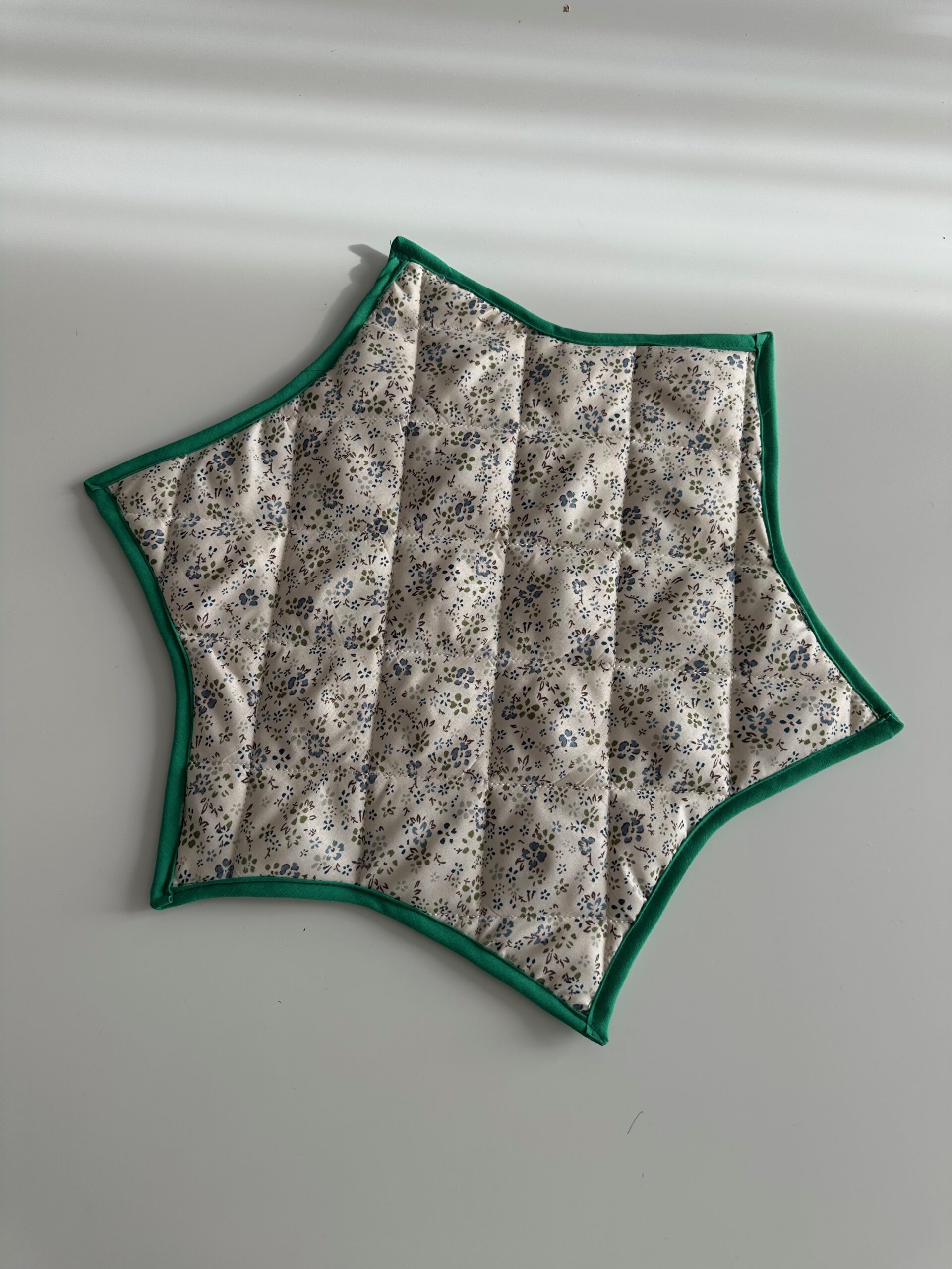 Quilted tree skirt and table topper in cream fabric with green binding, shown flat in its six-point star shape