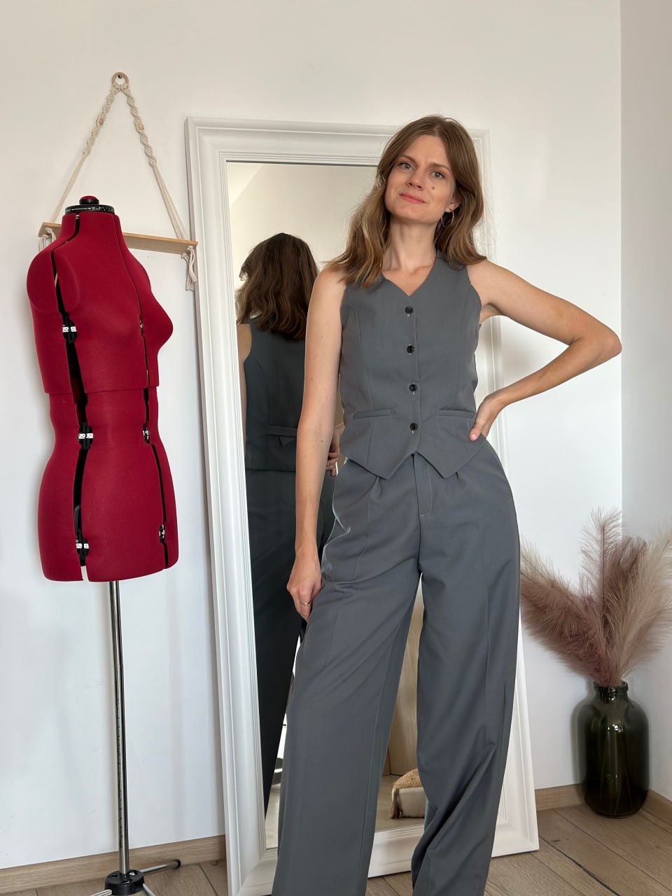 Grey tailored waistcoat worn buttoned with matching high-waisted wide-leg trousers — side view with the mirror showing the back